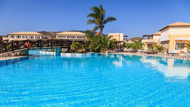 A large swimming pool with clear blue water, surrounded by palm trees and lounge chairs. - Natura Park Village Hotel & Spa  (Kos)