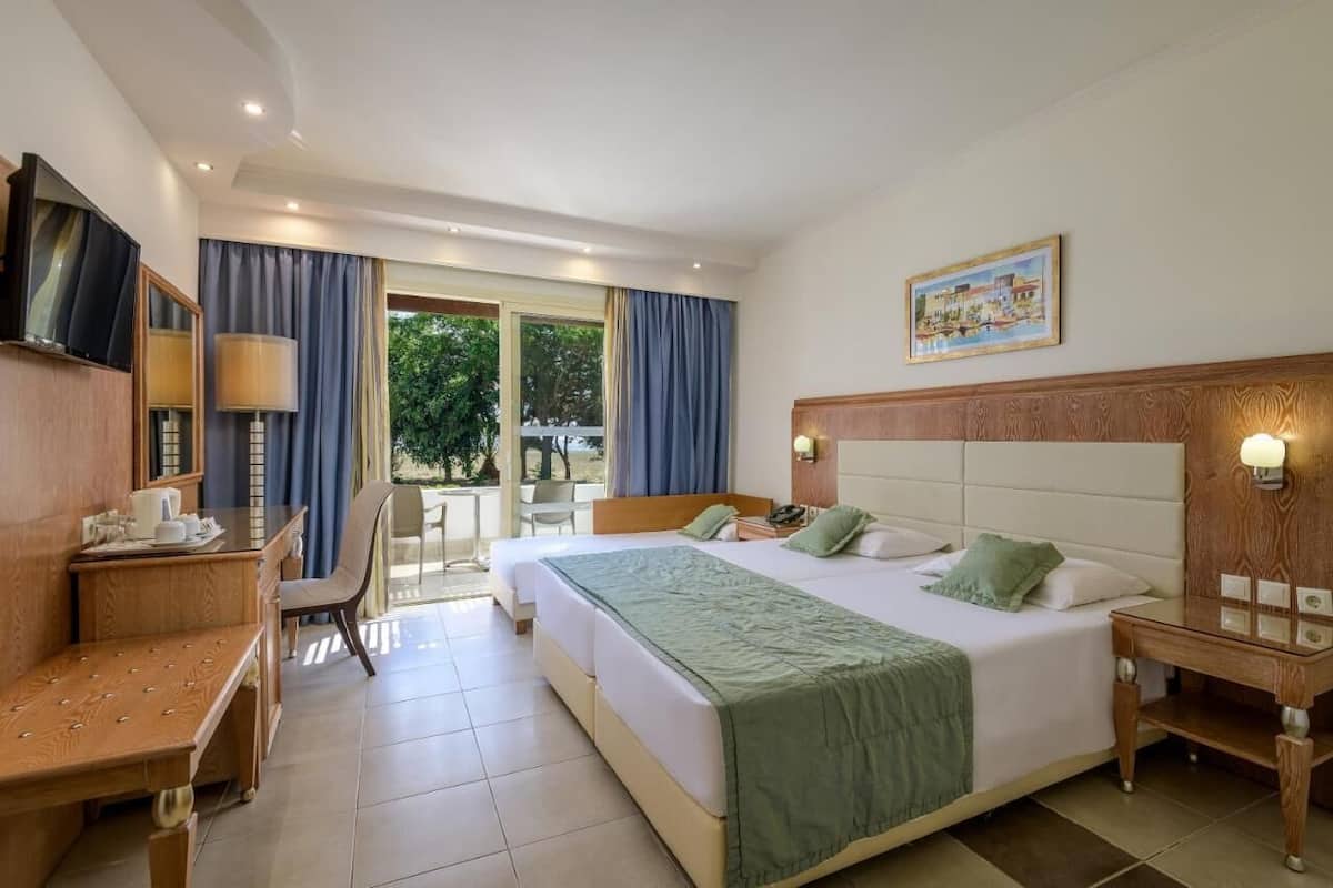 A hotel room with a large bed, a desk, a chair, a TV, and a balcony with curtains.