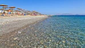 A beach with clear shallow waters, umbrellas, and sun loungers. - Natura Park Village Hotel & Spa  (Kos)