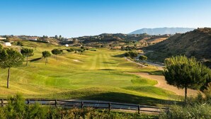 Un campo de golf con vista despejada al fairway, búnkeres de arena y una cadena montañosa distante.
