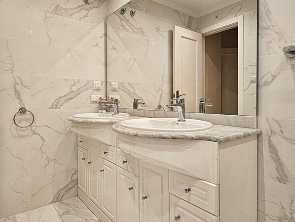 Une salle de bain avec deux lavabos, un grand miroir et des murs en marbre.