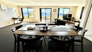 A dining area with a round table, six chairs, a clock, and a TV.