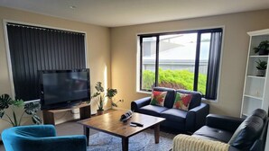 A living room with a TV, sofa, armchair, coffee table, and large windows.