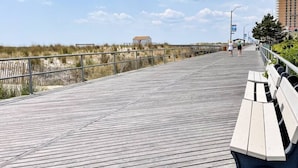 A wooden boardwalk with benches, a railing, and a view of the beach and buildings in the distance. - 7BR w/ Ocean Views + Onsite Parking + Central A/C (Ventnor City)
