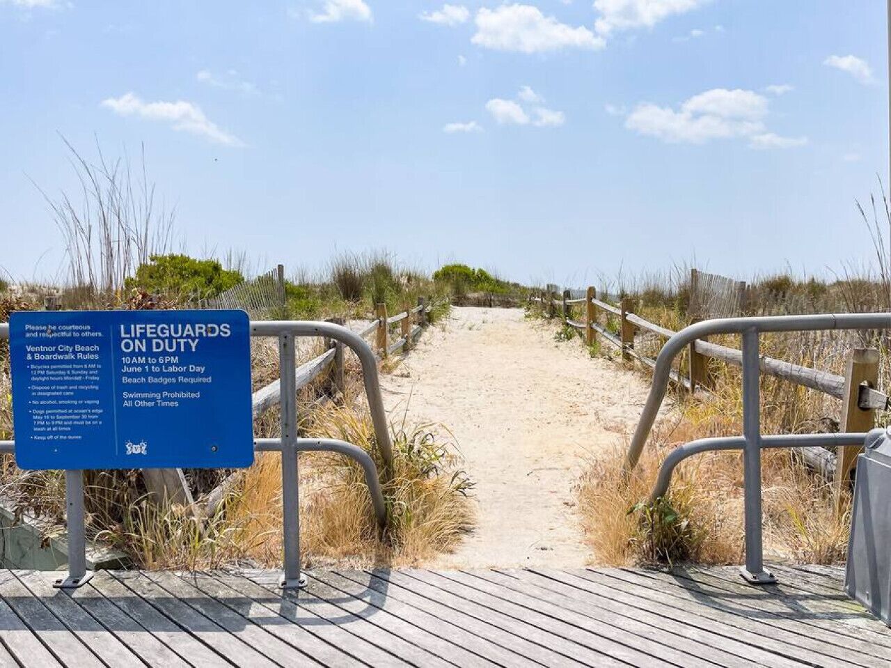 Un paseo marítimo de madera que conduce a una playa arenosa con un letrero de salvavidas.