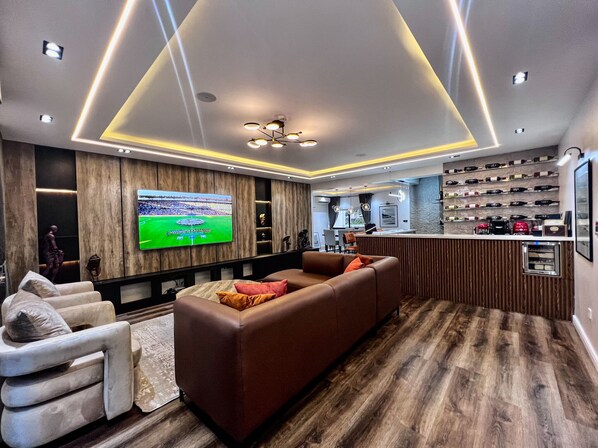 A modern living room with a large flat-screen TV, a brown sofa, a white armchair, and a wooden floor. - Luxury, Contemporary 4-bed Apartment in Ikoyi (Lagos)