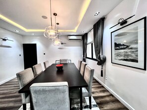 A modern dining room with a dark wooden table, grey upholstered chairs, a central red bowl, recessed ceiling lighting, and a framed black and white seascape on the wall. - Luxury, Contemporary 4-bed Apartment in Ikoyi (Lagos)
