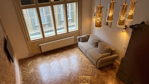 A modern living room with a herringbone floor, a sofa, a dining table with chairs, and a large window with multiple panes. - VISAJ Downtown (Timisoara)