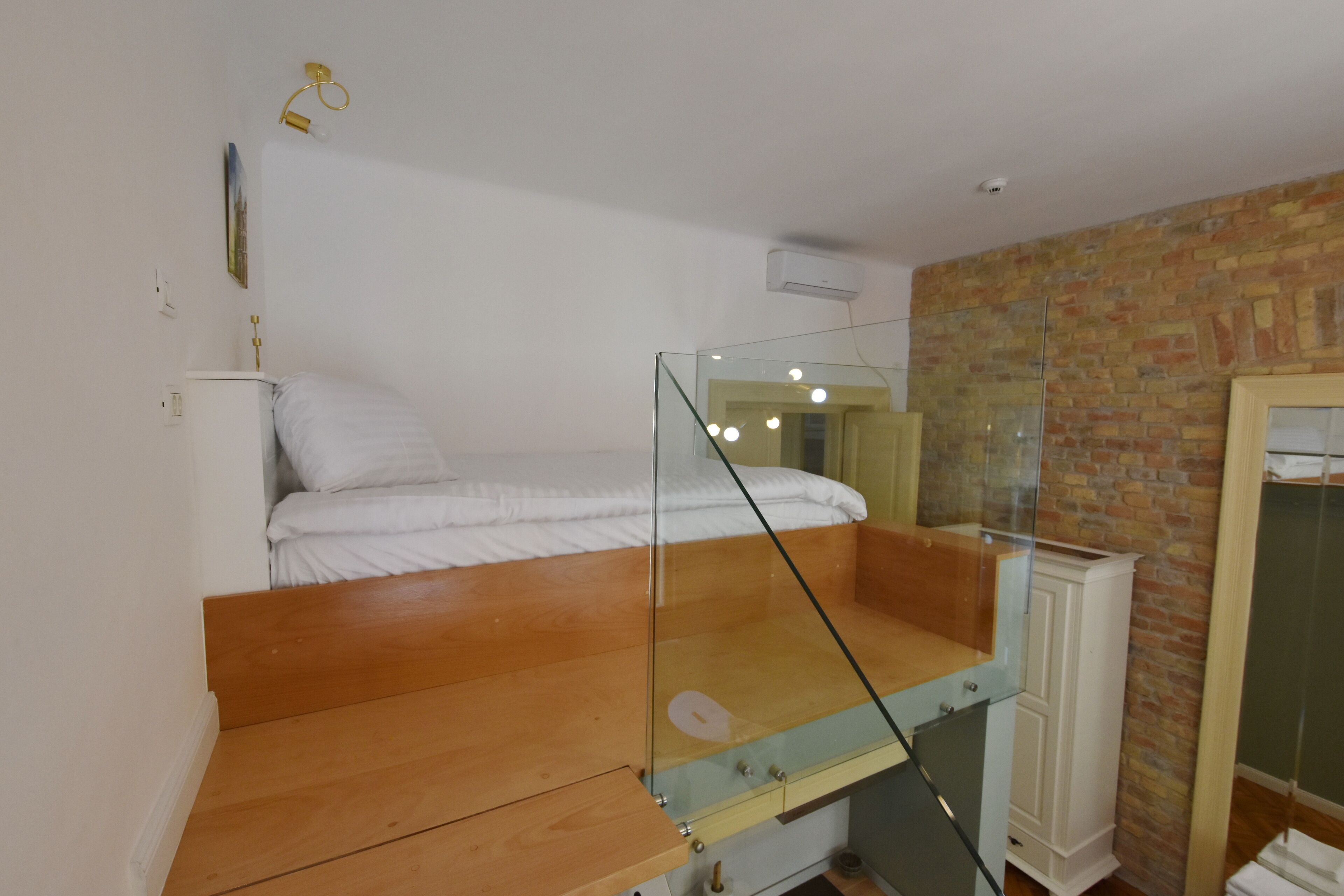 Et lille værelse med køjeseng, glasvæg, hvidt skab og murstensvæg.