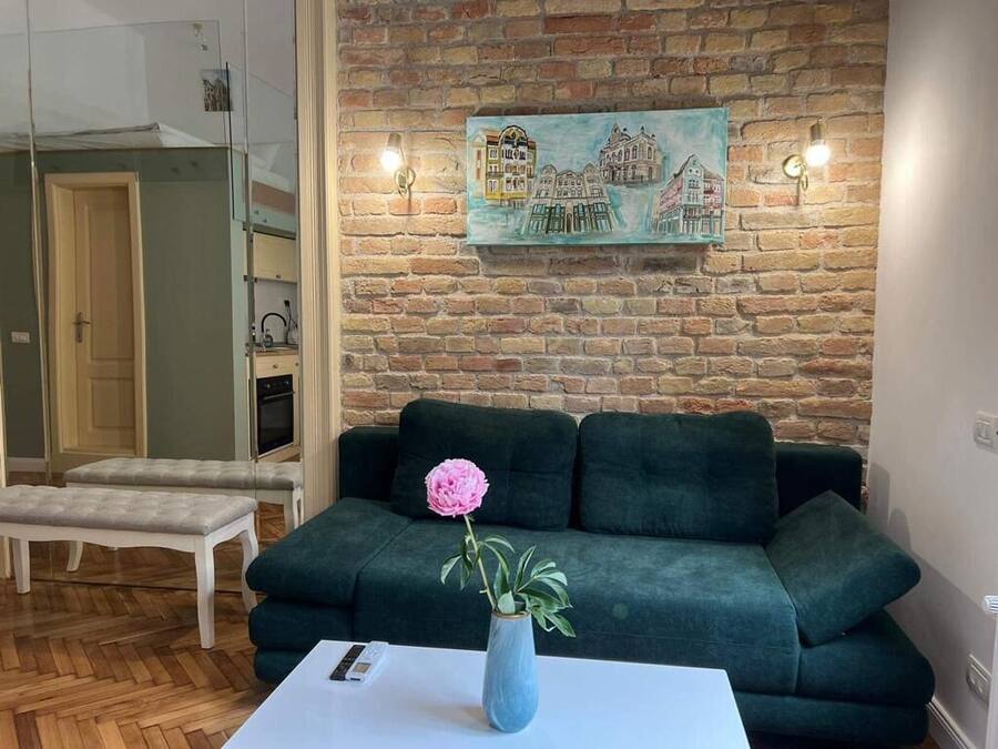 Een woonkamer met een groene bank, een witte salontafel met een vaas en een bloem, en een bakstenen muur met een schilderij.