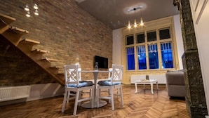 A dining area with a herringbone wooden floor, a brick wall, and a window with blue curtains. - VISAJ Downtown (Timisoara)