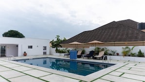 A rectangular swimming pool with a tiled deck, surrounded by lounge chairs and umbrellas. - No. 8 Boutique Hotel (Ilorin)