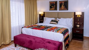 A hotel room with a large bed, a bedside table, a nightstand, a bench, and two paintings on the wall. - No. 8 Boutique Hotel (Ilorin)