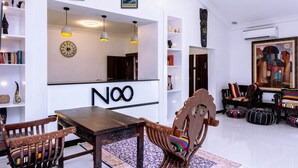 A modern living room with a dining area, featuring a wooden dining table, two chairs, a sofa, and a coffee table. There are shelves with decorative items and a large mirror on the wall. - No. 8 Boutique Hotel (Ilorin)