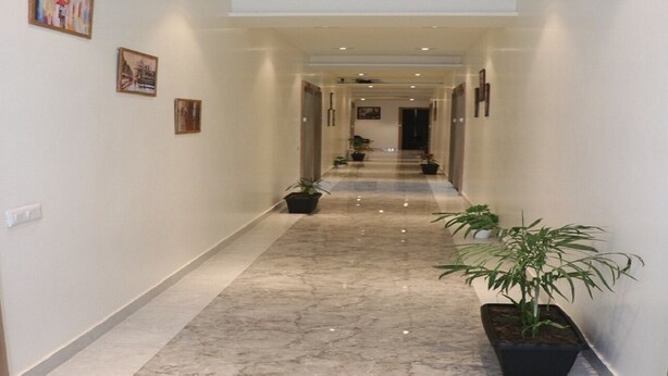 A hallway with marble flooring, potted plants, and framed artwork on the walls. - Signum CityScapes The Royal Jewel (Hisar)