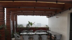 A covered outdoor patio with a tiled floor, a long table, and several wicker chairs. - Signum CityScapes The Royal Jewel (Hisar)