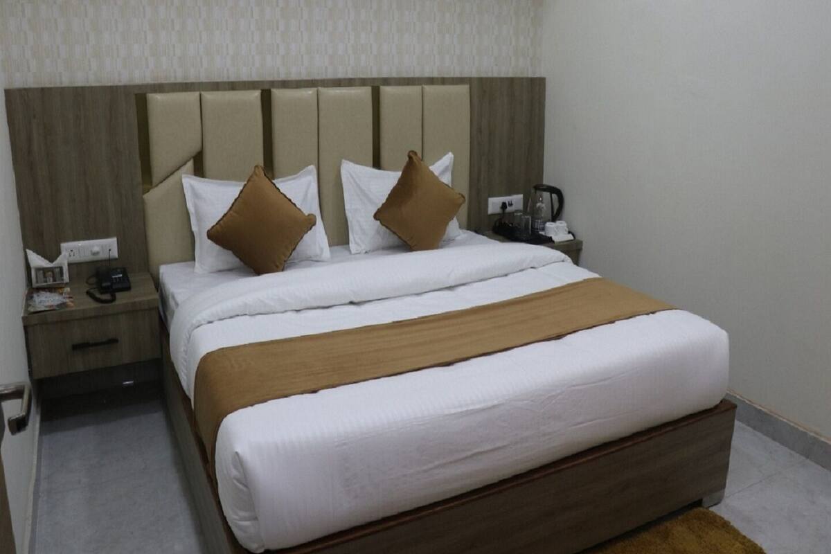 A neatly made bed with white linens and brown pillows, a wooden headboard, a bedside table with a phone and a lamp, and a small nightstand with a cup and a tissue box.