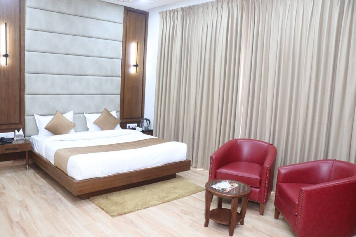 A hotel room with a large bed, two red leather chairs, a small round table, and a wooden nightstand.