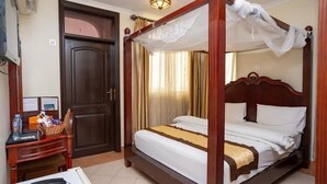 Una cama con dosel y cortinas, un escritorio con teléfono y una puerta cerrada.