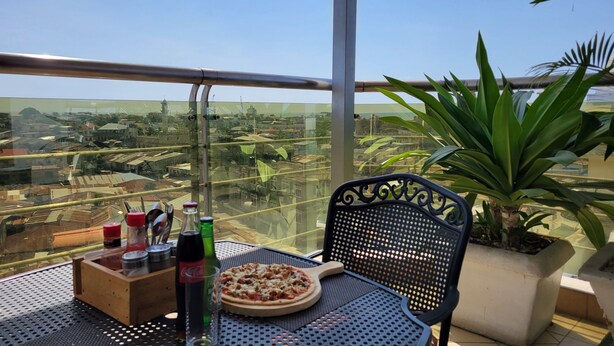 Un balcón con una mesa, una silla, una pizza y botellas de Coca-Cola y otra bebida.