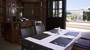 Comedor con una mesa dispuesta para dos, muebles de madera y vistas a través de un ventanal.