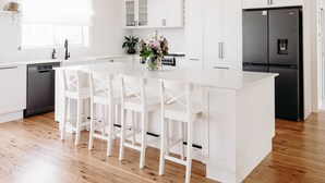 A modern kitchen with white cabinetry, a black refrigerator, and a central island with bar stools. - Centrally Located Spacious & Luxurious Cottage (Parkes)