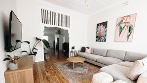 A modern living room with a wooden floor, a grey sofa, a coffee table, and various plants. - Centrally Located Spacious & Luxurious Cottage (Parkes)