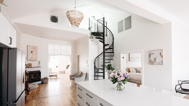 A spacious kitchen with a white island, wooden flooring, and a black spiral staircase. - Centrally Located Spacious & Luxurious Cottage (Parkes)
