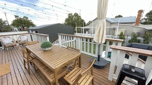 A wooden deck with a table and chairs, a potted plant, and a barbecue grill. - Centrally Located Spacious & Luxurious Cottage (Parkes)