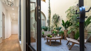 Un intérieur moderne avec un plancher en bois, une porte vitrée donnant sur un patio aménagé avec une table ronde, des chaises et des plantes en pot.