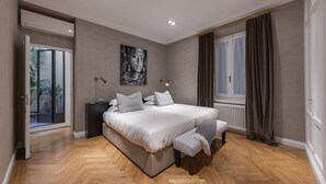 Une chambre à coucher moderne avec un grand lit, une table de chevet, une lampe sur pied et une fenêtre avec des rideaux.