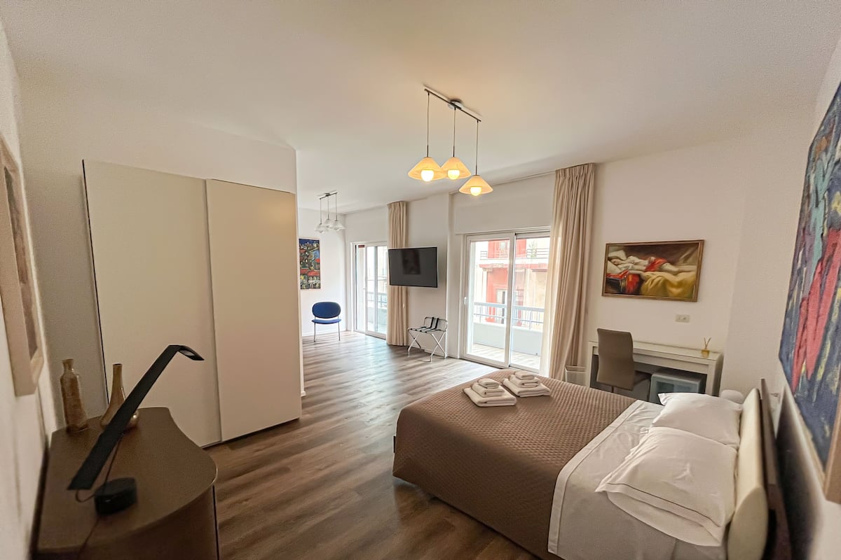 A hotel room with a bed, a desk, a chair, a TV, and a painting on the wall.