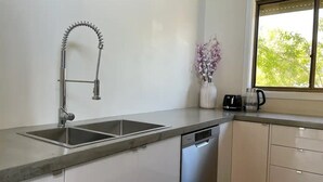 A modern kitchen with a double sink, stainless steel dishwasher, and a window with a view of greenery. - Close to the Coast & Bellarine Peninsula (Moolap)