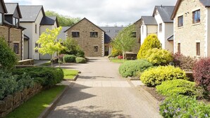 A residential area with stone houses, a paved driveway, and well-maintained gardens.
