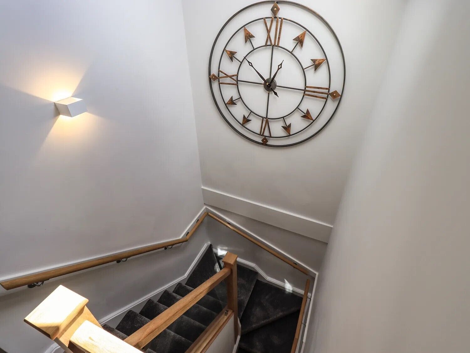 A staircase with a wall-mounted clock and a wall-mounted light fixture.