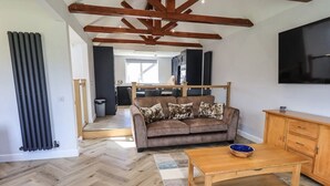 A living room with a herringbone floor, a brown sofa with patterned cushions, a wooden coffee table, and a TV mounted on the wall.