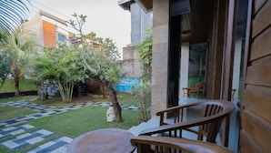 Un patio con una mesa redonda y sillas de madera, un sendero a cuadros y un pequeño jardín con diversas plantas y un árbol.