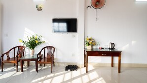 A dining area with a wooden table, chairs, a TV mounted on the wall, a fan, and a vase with flowers. - Loc Phat Hotel (Ho Chi Minh City)