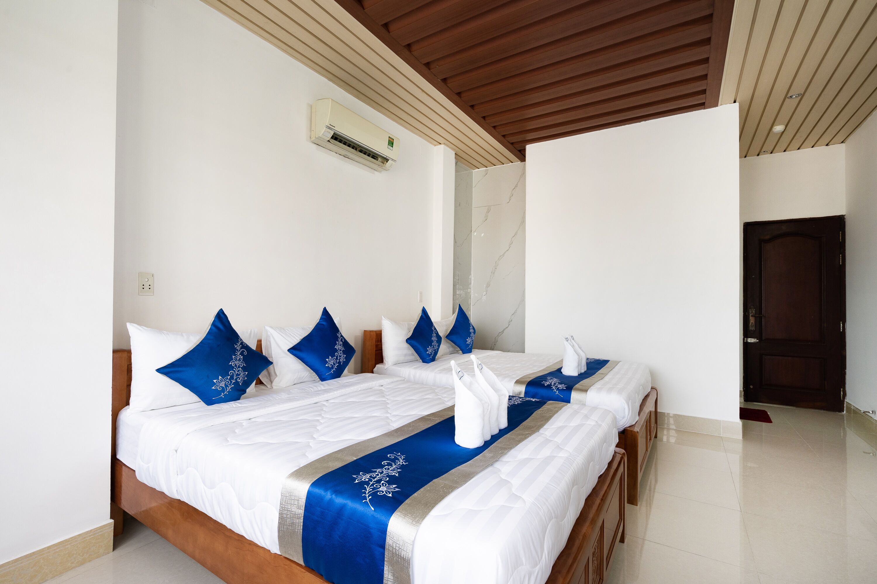 Una habitación de hotel con dos camas, ropa de cama blanca, almohadas azules y techo de madera.