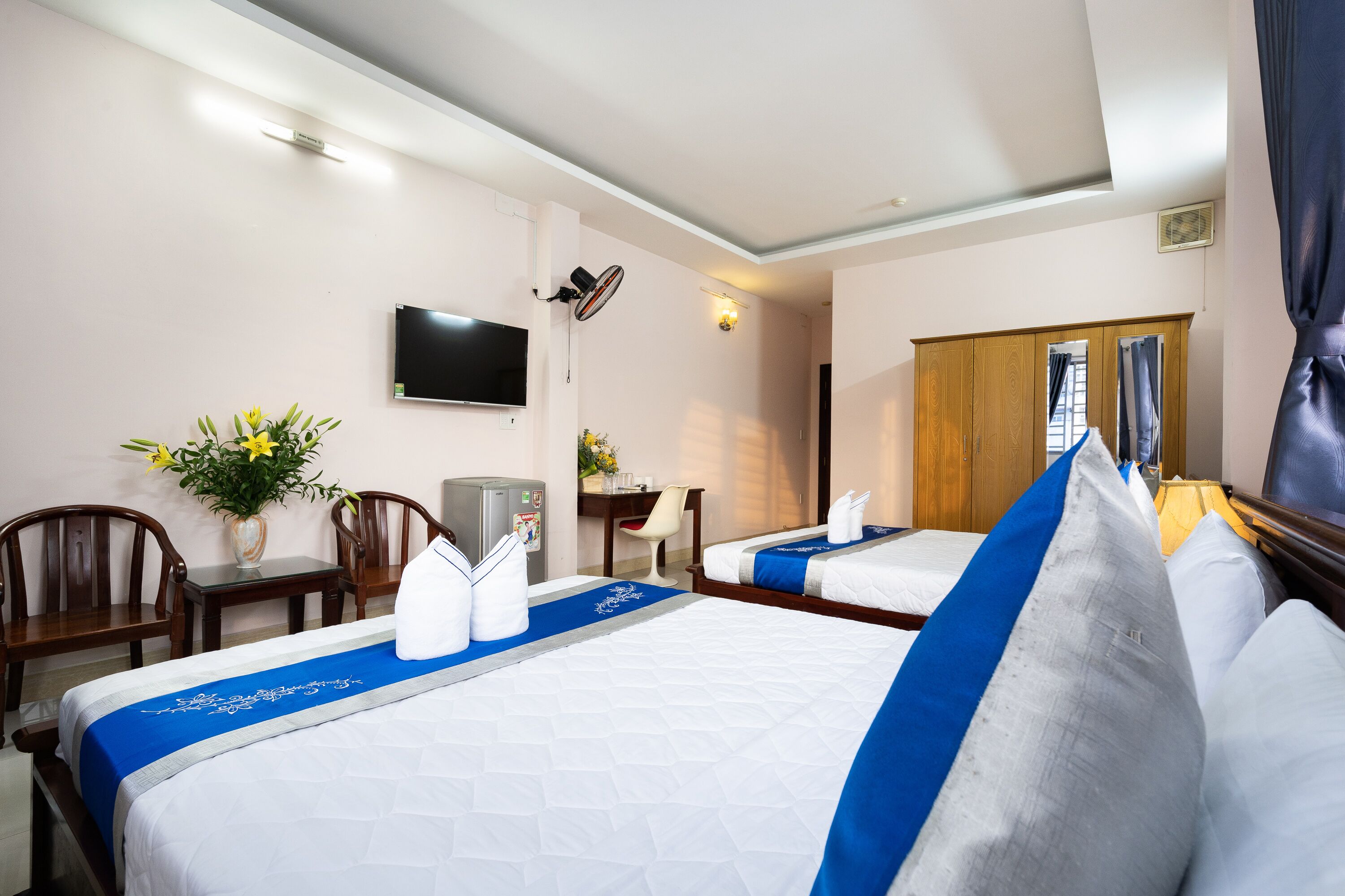 A hotel room with two beds, a desk, a chair, a TV, and a window with curtains.