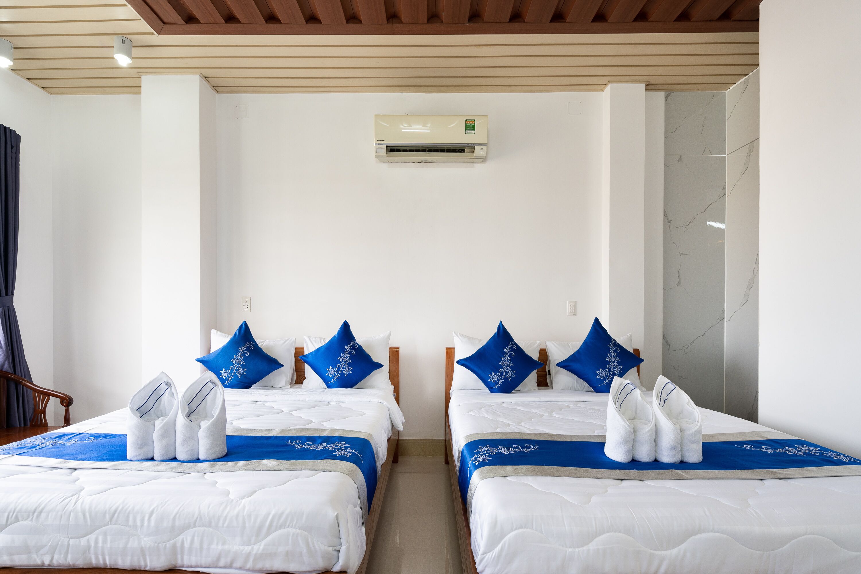 A hotel room with two beds, white bedding, blue pillows, and towels.