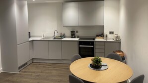 A modern kitchen with grey cabinets, a sink, and a dining area with a round table and chairs. - Salford City Retreat - Modern 2 Bedroom Apartment (Salford)