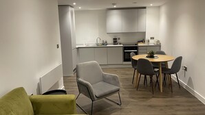 A modern kitchen with white cabinets, a dining area with a round table and chairs, and a green sofa in a living area. - Salford City Retreat - Modern 2 Bedroom Apartment (Salford)