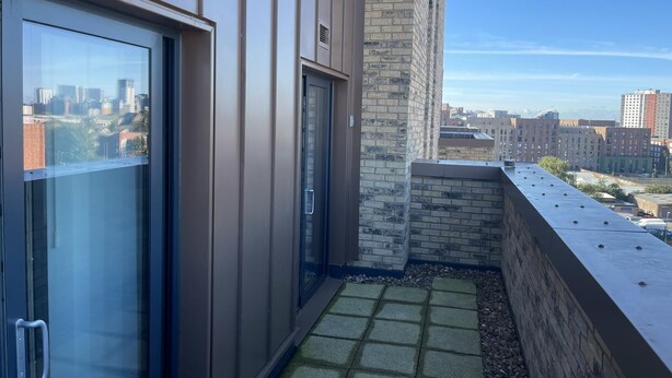A modern building with a glass door, a brick wall, and a view of a cityscape. - Salford City Retreat - Modern 2 Bedroom Apartment (Salford)