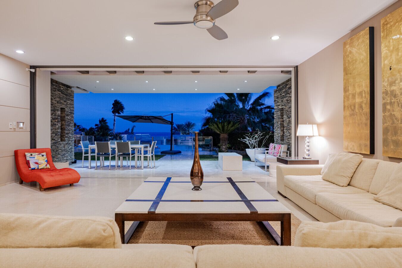 A modern living room with a sofa, a red chair, a coffee table, and a view of the outdoor patio area.