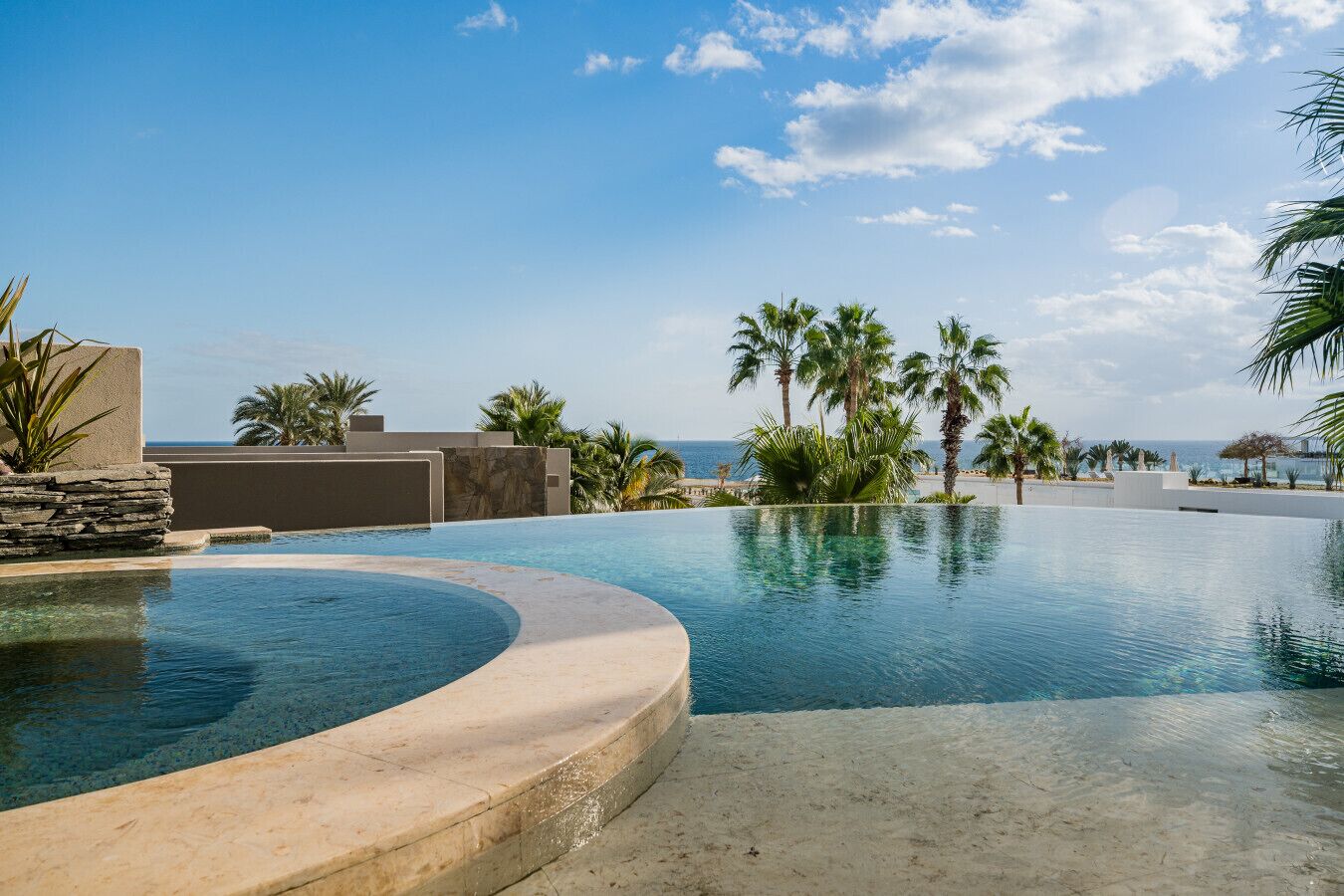 A resort pool with a curved edge, palm trees, and a view of the ocean.