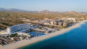 A coastal hotel with a large pool, beachfront, and mountainous backdrop.