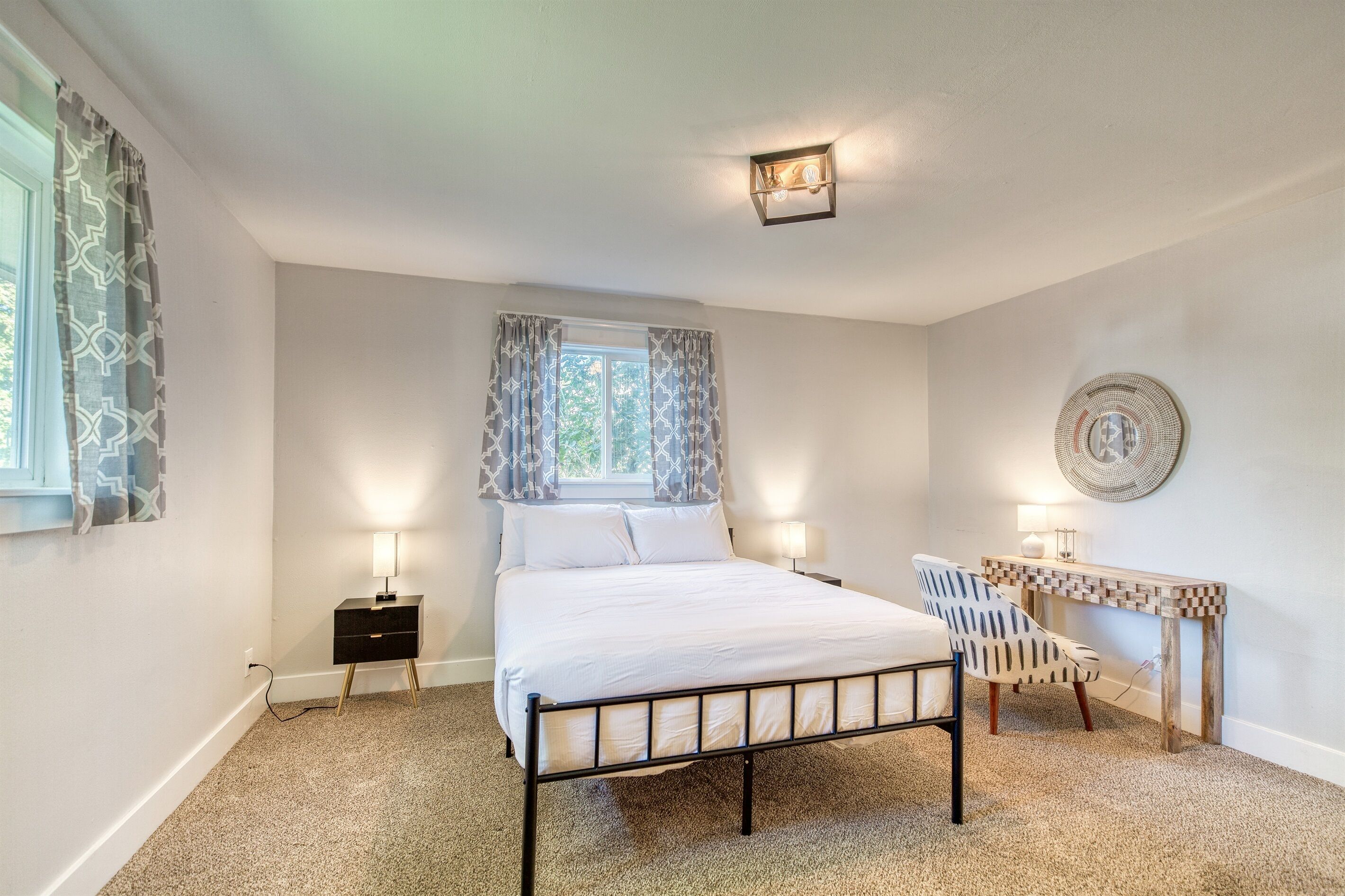 Ein Schlafzimmer mit einem Bett, Nachttischlampen, einem Sessel, einem kleinen Tisch und einem Wandventilator.