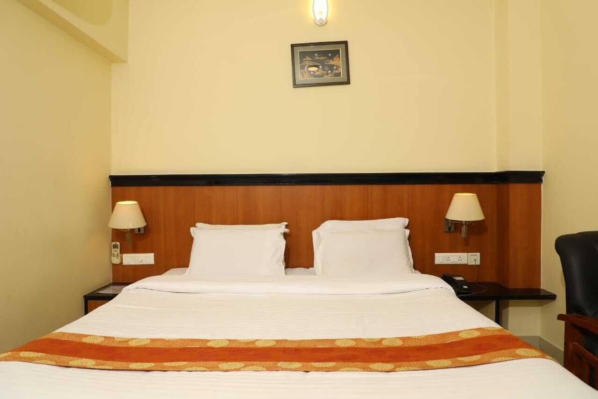 A hotel room with a wooden headboard, two bedside lamps, a bed with white linens, and a framed picture on the wall.