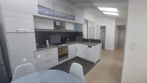 Moderni keittiö, jossa on valkoiset kaapit, liesi, uuni ja astianpesukone. Etualalla on ruokapöytä ja tuolit.